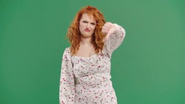 Hoşlanmayan kadın. Yüzünü buruşturan Hınzır Kadın Başparmaklarını Aşağı Gösteriyor. Yeşil stüdyo arka planında hoşnutsuzluğunu ifade eden güzel bir bayan. Yüksek kalite 4k