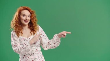 Gülümseyen 30 'lu yaşlardaki bayan reklam için boş bir yer arıyor. Önerilen kadın sol tarafı işaret ediyor, kopyala alanı. Kadın, yeşil arka planda izole edilmiş bir şey sunuyor. Yüksek kalite