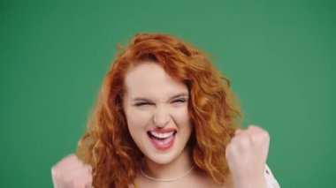 Kumral, 30 'lu yaşlarda, kendine güvenen bir kadın zafer işareti gösteriyor. Evet, zafere ulaştı. Hedeflerine ulaştı. Mutlu bir bayan, yeşil arka planda heyecanlı bir sürpriz. Büyük ikramiye konsepti. Yüksek kalite