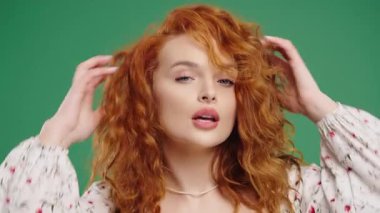 Doğal kızıl bukleli çekici bir kadın, objektife bakarken saç stilini değiştiriyor. Güzellik, kendine güven, kişisel bakım, moda veya yaşam tarzı içeriği