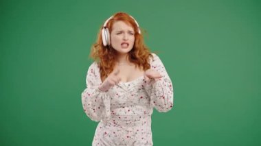 Kıvırcık Amerikalı kadın kafayı buluyor, müzik dinliyor, yeşil stüdyo arka planında kulaklıklarla dans etmekten zevk alıyor. Radyo, kablosuz modern ses teknolojisi, çevrimiçi çalar. Yüksek kalite 4k