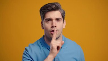 Sessiz, sessiz, komplo, sessiz, söylenti konsepti olan yakışıklı bir adam. Gülümseyen adam parmaklarını dudağında tutuyor, sarı stüdyo geçmişi var. Yüksek kalite 4k