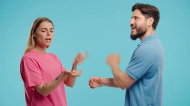 Mavi arka planda duygusal olarak kavga eden genç bir çift. Çatışma kavramı, ilişkilerde sorunlar. Beyaz Amerikalı kadın ve erkek. Yüksek kalite 4k görüntü