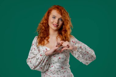 Güzel bir kadın elleriyle kalp şekli oluşturur, sevgi gönderir. Yeşil arka planda güzel kıvrımlı bir bayan. Kadın sağlığı, gönüllülük, bağış, minnettarlık sembolü, flört. Yüksek kalite