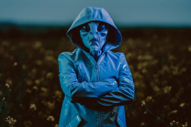 Yeşil neon ışıklarının altında ürkütücü bir uzaylı var. Korkunç bir maske, vinil pürüzsüz bir yağmurluk. UFO, dünya dışı yaşam, cadılar bayramı kostümü konsepti. Yüksek kalite fotoğraf