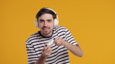 TV 'de video oyunu oynayan yakışıklı esmer adam sarı stüdyo arka planında joystick izole edilmiş. Modern teknolojiyi kullanarak.