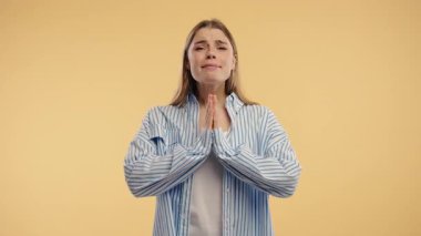 Bej renkli stüdyo arka planında dua eden hoş bir kadın. Vücut pozitifliği olan kadın, birine arzularını tatmin etmesi için yalvarır, yardım eder, şans için dua eder. Yüksek kalite 4k