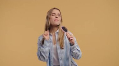 Pijamalı neşeli sarışın kadın mikrofon gibi saç fırçasında şarkı söylüyor, parlak stüdyoda neşeyle dans ediyor. Neşeli ruh hali, mutluluk, kendini ifade etme, eğlenceli sabahlar, kaygısız yaşam tarzı, kadın güveni.