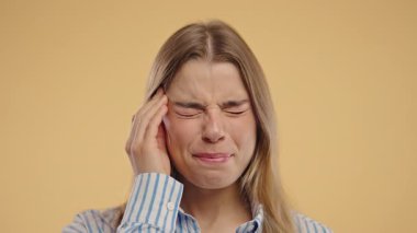 Baş ağrısı, kan basıncı, stüdyo fotoğrafı olan genç bir kadın. Kafasında elleri olan, izole edilmiş bej arka planı olan bir kadın. Sorunlar, migren semptomları, hastalık. Yüksek kalite 4k