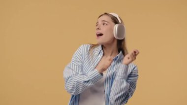 Mutlu kadın kafayı bulur, müzik dinler, bej renkli stüdyo arka planında kulaklıklarla dans etmekten zevk alır. Radyo, kablosuz modern ses teknolojisi, çevrimiçi çalar. Yüksek kalite 4k