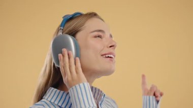 Amerikalı kadınlar kafayı bulur, müzik dinler, bej renkli stüdyo arka planında kulaklıklarla dans etmekten zevk alır. Radyo, kablosuz modern ses teknolojisi, çevrimiçi çalar. Yüksek kalite 4k