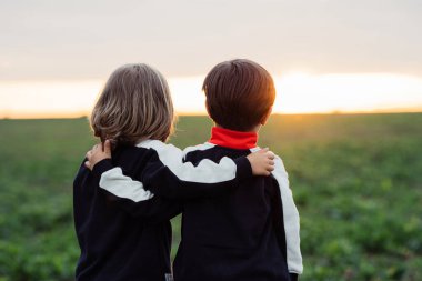 Gün batımını izleyen çocuklara sarılmak, Meadow Doğa 'nın arka planındaki ufka bakmak. Yüksek kalite fotoğraf