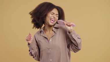 Oyuncu Afrikalı Kadın Şarkı Söylüyor, Mikrofon yerine Saç fırçasıyla Dans Ediyor. Melez bir bayan eğleniyor, müzik dinliyor, karaoke yapıyor, ünlü olma hayalleri kuruyor. Yüksek kalite 4k görüntü