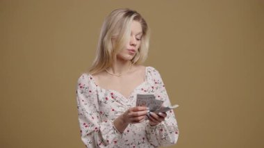 Zengin, nakitli, güzel bir kadın. Bej duvarda Amerikan Doları banknotları. İkramiye, kazanç, zafer, kazanan piyango, maaş sembolü. Yüksek kalite 4k