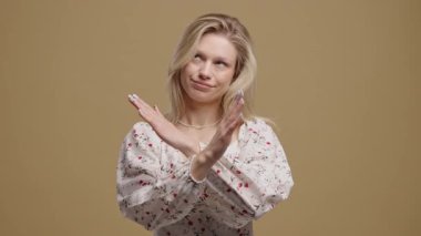 Hayır, asla, güzel sarışın Amerikalı genç kız el işaretini keserek jesti reddediyor ve ondan hoşlanmıyor. Onaylamayan hoş bir kadın bej renkli stüdyo arka planında inkar işareti yapıyor. Ban, mola. 4k