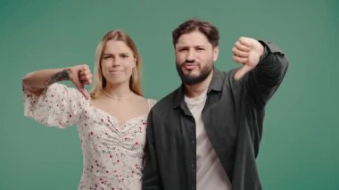 Mutsuz kadın ve erkeğin portresi, hoşlanmama işaretiyle kınanır. Yeşil stüdyo arka planında olumsuz jest yapan çift hoşnutsuzluğunu dile getiriyor.