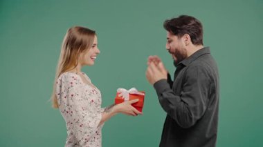 Yeşil arka planda genç bir çift. Beyaz Kadın, kocasına ya da erkek arkadaşına yay ile hediye veriyor. Doğum günü, kutlama, sürpriz, yıldönümü konsepti. Yüksek kalite 4k