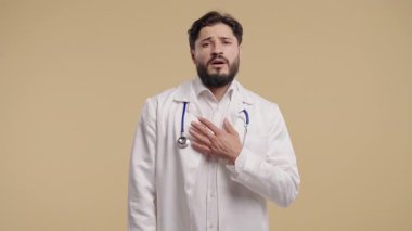 Beyaz önlüklü genç erkek doktor kameraya empatik bir ifadeyle bakıyor, hastayı dinliyor. Stüdyo fotoğraflarında tıbbi uzmanlar destek, ilgi ve ilgi gösteriyor. Yüksek kalite 4k görüntü