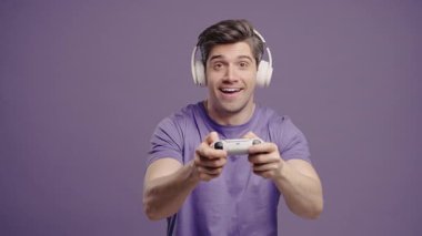 Violet stüdyosunun arka planında joystick izole edilmiş video oyunu oynayan yakışıklı esmer adam. Modern teknolojiyi kullanarak.