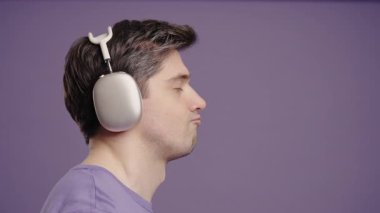 Olumlu beyaz Avrupalı adam müzik dinliyor, Violet stüdyosunun arka planında kulaklıklarla dans ediyor. Radyo, kablosuz modern ses teknolojisi, çevrimiçi çalar. Yüksek kalite 4k