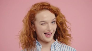 Çekici genç bayan kameraya neşeli bir şekilde göz kırpıyor yumuşak bir gülümseme, kendine güven ve hafif bir flörtle. Cazibe, bağlantı, eğlence, doğal kendini ifade etme temaları için harika.