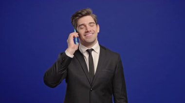 Olgun gülümseyen, olgun Amerikan Yöneticisi CEO patron telefonla konuşuyor, hoş bir şaka, gülümsüyor. Mavi arka plandaki genç adam. Akıllı telefon görüşmesi. Yüksek kalite 4k