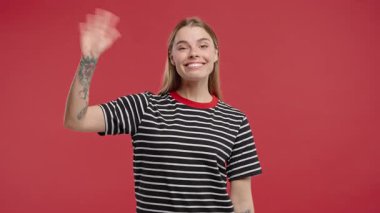 Dost canlısı genç Amerikalı kadın el sallıyor - merhaba, selam, kaos, adios. Ayrılıyorum, kameraya hoşça kal de. Kırmızı stüdyo arka planındaki güzel bayan. Yüksek kalite 4k
