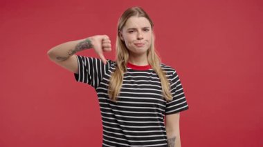 Mutsuz Amerikan kadınlarının portresi, hoşlanmama işaretiyle kınanıyor. Yetişkin bir kadın, kırmızı stüdyo arka planında baş parmağını göstererek memnuniyetsizliğini dile getiriyor..