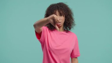 Mutsuz bir Afrikalı Amerikalı kadının portresi sevmeme belirtileriyle kınanıyor. Genç bir bayan, mavi stüdyo arka planında olumsuz bir hareket göstererek memnuniyetsizliğini dile getiriyor..