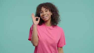 El işaretli afro-amerikan kadın, tamam jest. Mutlu bayan, doğru seçim, harika bir anlaşma, mavi arka plan. Pozitif kadın model kameraya gülümser, onay, güven konsepti. 4k