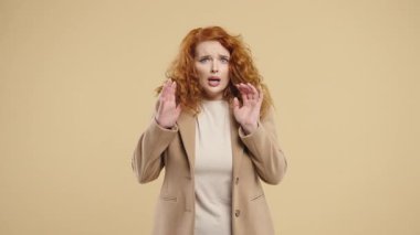 Young Woman frightened shocked afraid of something and screaming into camera with big eyes full of horror on beige background. Phobia, trouble, panic concept. High quality 4k footage