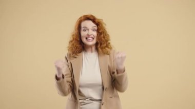 Excited auburn-haired 30s woman shows triumph yes gesture of victory, she achieved result, goals. Lady glad, surprised excited on beige background. Jackpot concept. High quality 4k