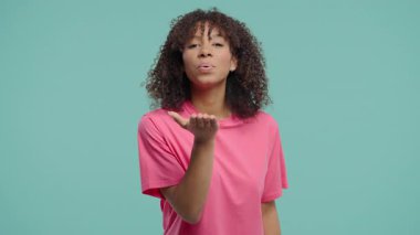Neşeli Afrikalı Kadın Gülümsüyor, Mavi Stüdyoda Kameraya Flört Ediyor. Çekici trend kızı muhteşem kıvırcık saçlarını düzeltiyor. Yüksek kalite 4k görüntü