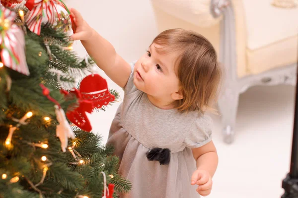 一个穿着灰色衣服的小女孩用一个球装饰圣诞树 — 图库照片