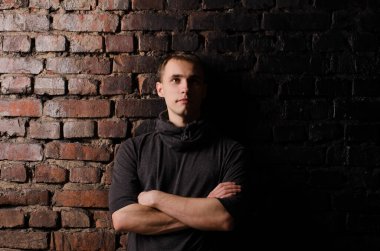 Siyah ceketli bir gencin portresi kahverengi, kırmızı ve siyah tuğlalı bir duvarın arkasında.