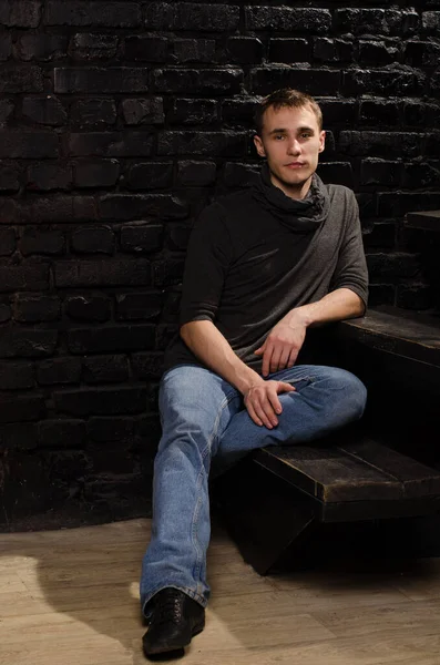 一个穿着黑色毛衣坐在台阶上靠着砖墙坐着的年轻人的画像 — 图库照片