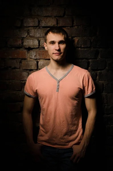 一个穿着粉色T恤衫的年轻人站在砖墙边 工作室照明的画像 — 图库照片