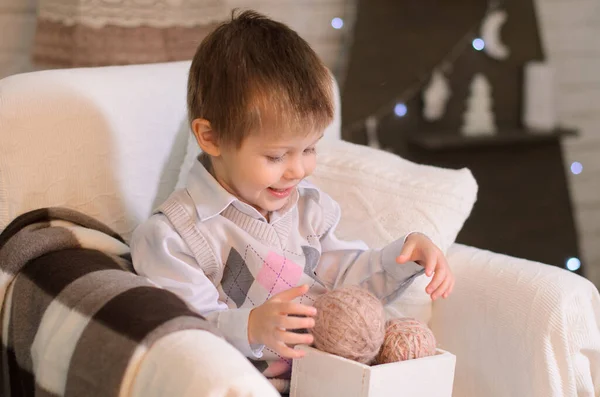 一个笑着的小男孩的画像 他坐在舒适的房间里的扶手椅上 正在检查一个盒子里编织的纱球 — 图库照片