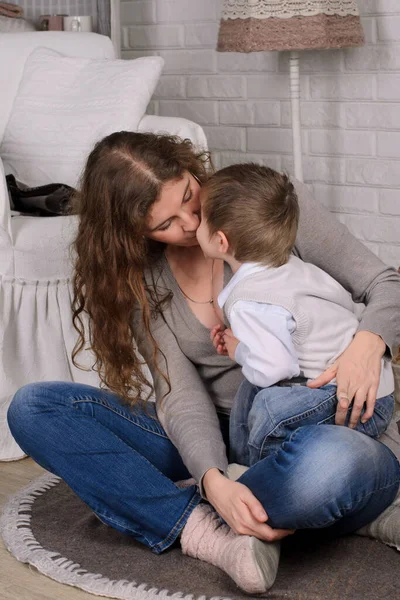 portrait of mother and son hugging and kissing, sitting on the floor in the room, casual clothing style