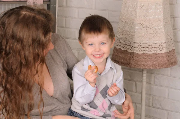 小男孩笑着 坐在妈妈的怀里 吃着百吉饼 在房间里 — 图库照片