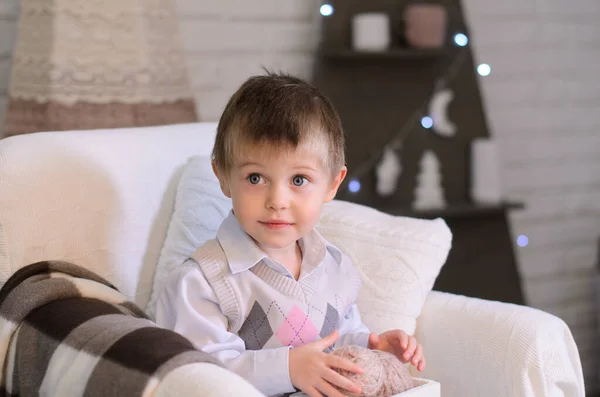 一个小男孩的画像 手里拿着一个纺纱球在一个盒子里编织 坐在一个舒适房间的扶手椅上 — 图库照片