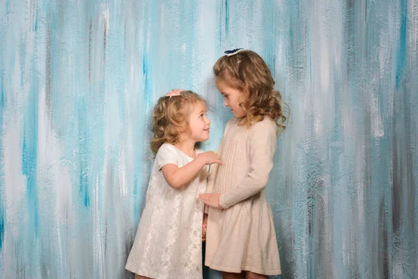 两个漂亮的微笑的女孩 穿着浅色衣服的姐姐们 在一道水彩画般的蓝色墙壁的后面交流着 — 图库照片