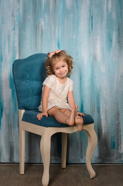 美しい光の服の少女は 水彩画のスタイルで青い壁に対して 古いヴィンテージの椅子に座っています — ストック写真