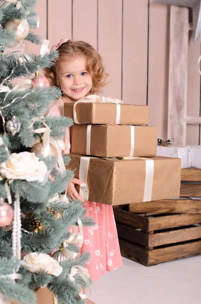 一个美丽的微笑的女孩从一棵装饰过的圣诞树后面向外张望 手里拿着三盒礼物 — 图库照片