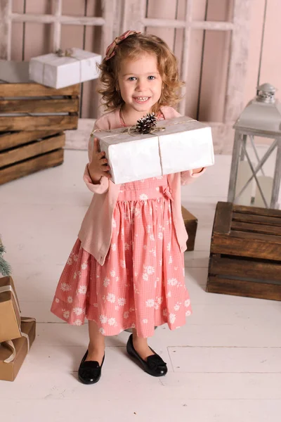 ピンクのお祝いのドレスと黒い靴を着て白い床に立ち手に贈り物の入った箱を手にロフトの木の壁を背景に — ストック写真