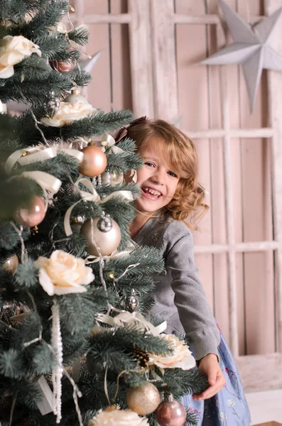 Egy Gyönyörű Nevető Lány Padlón Játékosan Kukucskál Díszített Karácsonyfa Mögül — Stock Fotó
