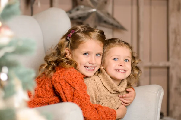 身着红米黄色毛衣的姐妹们 坐在扶手椅上拥抱在一起 在圣诞节的房间里 — 图库照片
