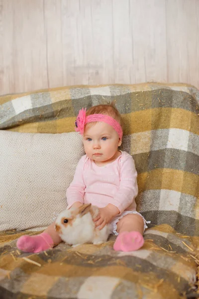 小さな女の子は小さな手でふわふわのウサギを愛撫しながら 小切手の毛布の上に座っています — ストック写真