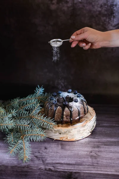 Egy Kézzel Porított Cukrot Szórnak Egy Csokis Muffinra Áfonyával Díszítve Stock Kép