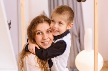 Odanın içinde gülümseyen bir anneye sarılan mutlu bir çocuğun portresi.